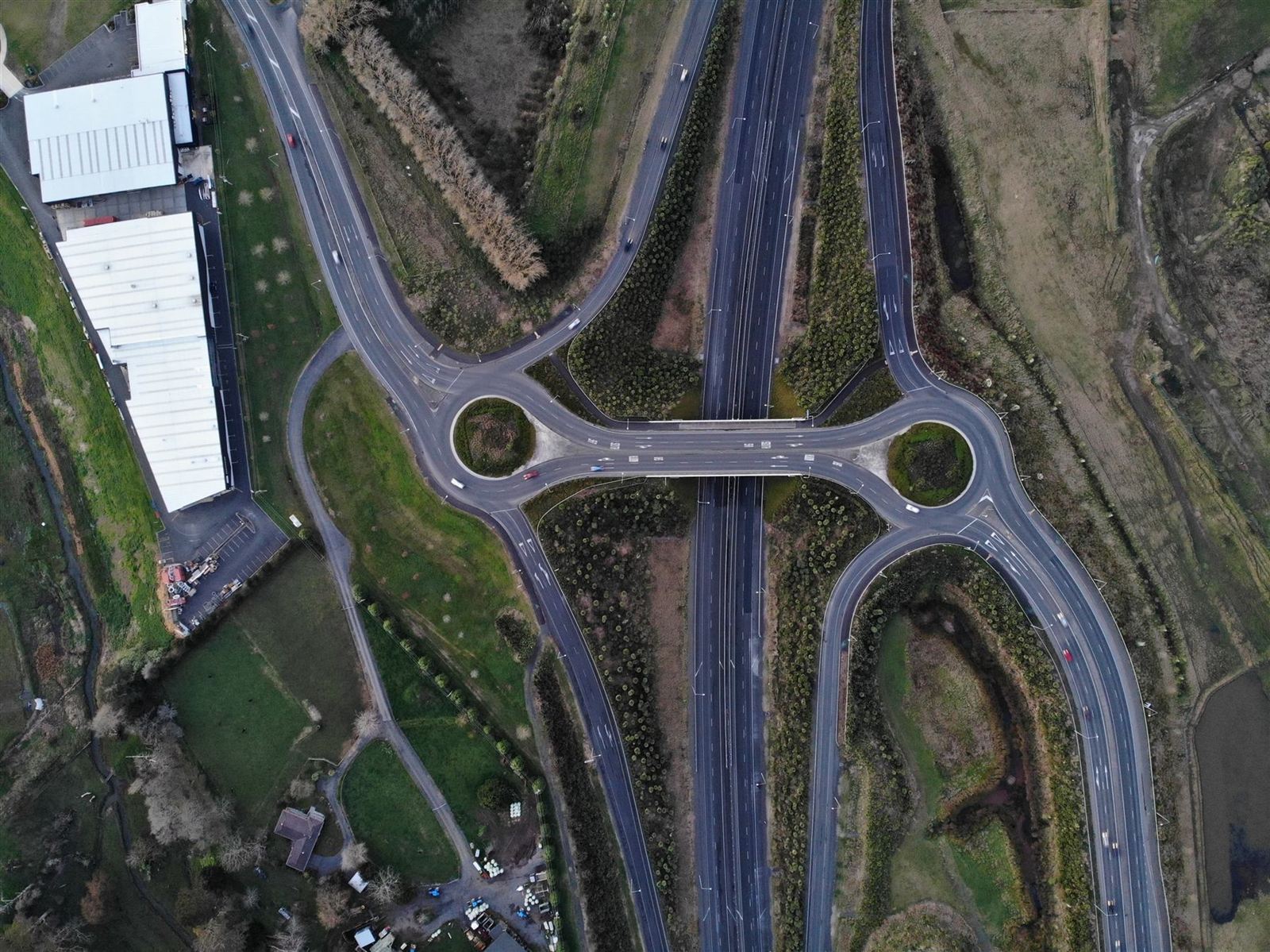 Aerial view of a motorway junction with roundabouts, landscaping and adjacent industrial units