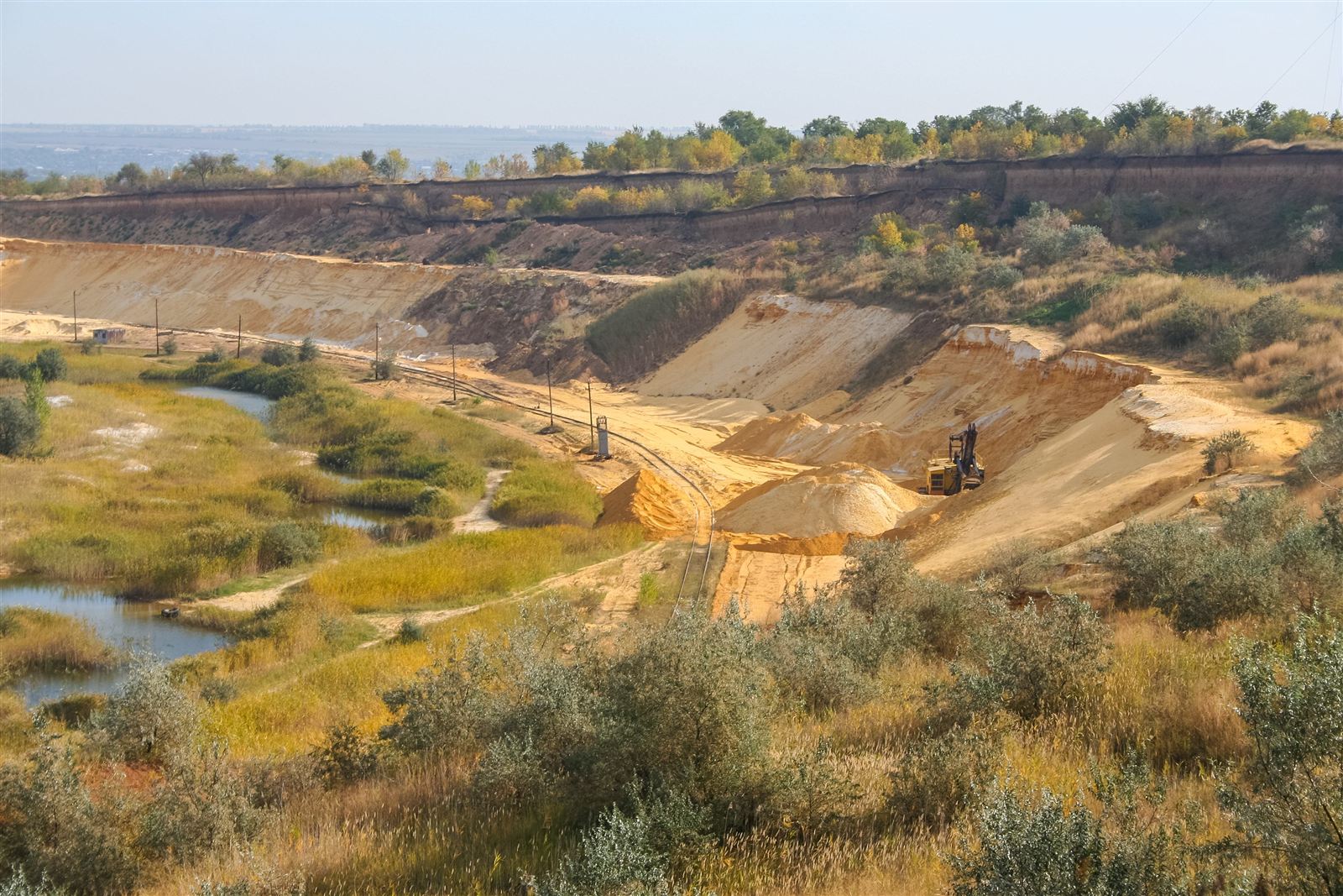 A sand quarry with an excavator, stockpiles and a wetland area in the foreground